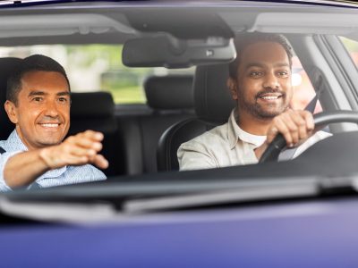 driver courses and people concept - happy smiling car driving school instructor teaching young man to drive